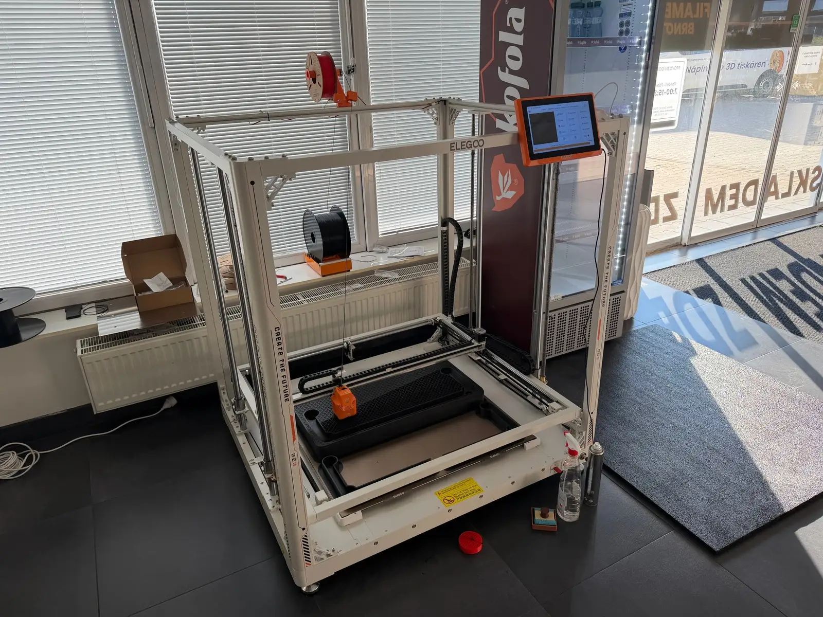 Velkoformátová 3D tiskárna Elegoo u okna uvnitř prodejny